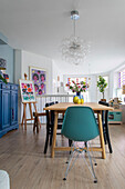 Dining room with petrol-coloured chair, wooden table and colourful decoration