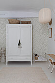 White vintage wardrobe in front of patterned wallpaper in a bright children's room