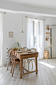 Light-coloured dining area with rustic wooden table and white curtains