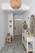 Hallway with patterned floor tiles, rattan lamp and white sideboard