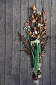 Flowering tazette daffodil bulbs on a wooden floor decorated with dried copper beech, fern, and larch branches