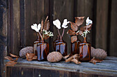 White cyclamen and baby's breath flowers in small brown glass bottles, decorated with dried copper beech leaves