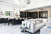 Open-plan kitchen with black cupboards, dining area and light-coloured couch in the adjoining living area