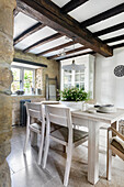 Country-style dining table in light-colored wood with ceiling beams and stone walls