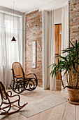 Schaukelstühle und Zimmerpflanze neben Ziegelwand im hellen Wohnraum
