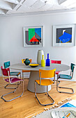 Ovaler Esstisch mit bunten Stühlen, darüber moderne Kunst an der Wand