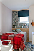 Bett mit rot karierter Tagesdecke, dahinter Ablage aus Sperrholz und Tapete mit Fischmotiv