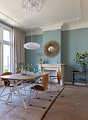 Essbereich mit Holztisch, Stühlen, Hängelampe und Spiegel an pastellblauer Wand