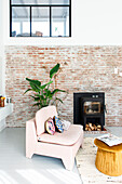 Reading corner in the loft-style living room with brick wall, pink armchair and modern fireplace