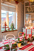 Christmas table setting with red candles and Christmas tree miniatures on the windowsill