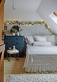 Bedroom in the attic with blue chest of drawers and fairy lights