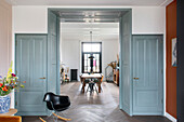 Durchgang mit grau-blauen Holzvertäfelung, flankiert von farblich passenden Türen, mit Blick ins Esszimmer