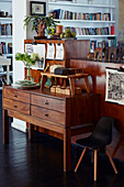 Vintage Holzkommode mit Kunst und Pflanzen dekoriert, im Hintergrund Bücherregal