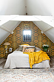 Schlafzimmer mit gemusterter Tapete, Dachschrägen und gelber Decke auf Bett