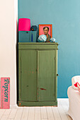 Green vintage cupboard with decorative objects in front of blue wall next to popcorn sign