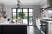 Moderne Küche mit schwarzer Kücheninsel, grauen Wänden und Blick in den Garten