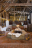 Festively laid table in a rustic barn setting with bales of straw and candlelight