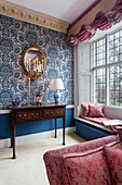 Antique console and wall mirror in front of blue and white patterned wallpaper
