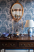 Antique wooden table with candles and lamp in front of blue and white wallpaper