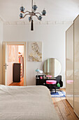 Double bed and white wardrobe in the bedroom, black dressing table and pink stool in the background