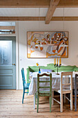 Country-style dining area with colourful wooden chairs and artwork on the wall
