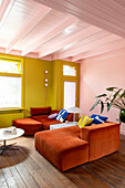 Living room with orange sofas, green and pink wall and houseplant