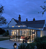 Glazed dining area and kitchen at dusk in renovated heritage farmhouse