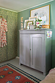 Grauer Schrank mit Dekoration und Bildern, grüne Wand, gemusterte Tapete
