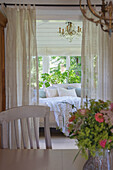 View through curtains to bed in bright bedroom with houseplants