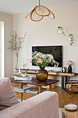 Wohnzimmer mit zentralem Couchtisch, Blumenarrangement und Hängeleuchte aus Rattan
