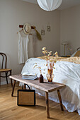 Bedroom in natural tones with wooden bench, dried flowers and woven bag