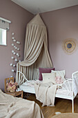 Kinderbett mit Baldachin und Kuscheltieren in einem rosa Kinderzimmer