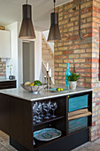 Kücheninsel mit modernen Pendelleuchten neben rustikaler Ziegelwand