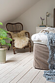 Attic bedroom with white wooden floor, vintage chair, fur and plant
