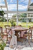 Gedeckter Tisch im Wintergarten mit Blick auf blühende Wiese