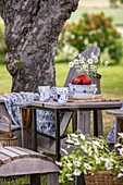 Gartentisch mit Geschirr und Blumenstrauß aus Margeriten im Sommer