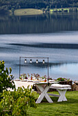 Gedeckter Tisch am See mit Blumenschmuck und Hängeleuchten