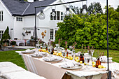 Gedeckter Tisch für ein Gartenfest mit Hängelampen und weißem Landhaus im Hintergrund