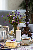 Gedeckter Tisch mit Kuchenstück, Teekanne und Wildblumenstrauß