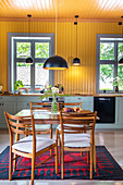 Holztisch und Stühle in Küche mit gelber Wand und schwarzer Pendelleuchte