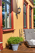 Veranda mit Liegestuhl und Topfpflanzen, gelbe Holzfassade