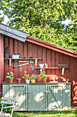 Werkzeuge und Blumentöpfe an einem roten Holzhaus im Sommer