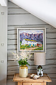 Painting on the wall, vase on chest of drawers, pitched roof with wood panelling
