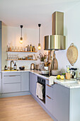 Moderne Küchenzeile mit Pendelleuchten, goldener Dunstabzugshaube und Dekor in Naturtönen