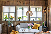 Wohnzimmer mit Holzwänden, Fensterfront und Hängeleuchte im skandinavischen Stil