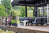 Terrasse mit Loungemöbeln und Blumen vor schwarzem Holzhaus