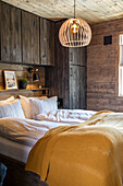 Holzvertäfeltes Schlafzimmer mit Hängeleuchte und Bett mit gelber Tagesdecke
