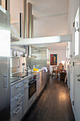 Modern, narrow kitchen with stainless steel appliances and dark wooden floor