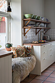 Kitchen corner with wooden shelves, tiled floor and seating area with fur and cushions