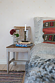 Chair as bedside table with candle and flowers next to bed with ethnic cushions